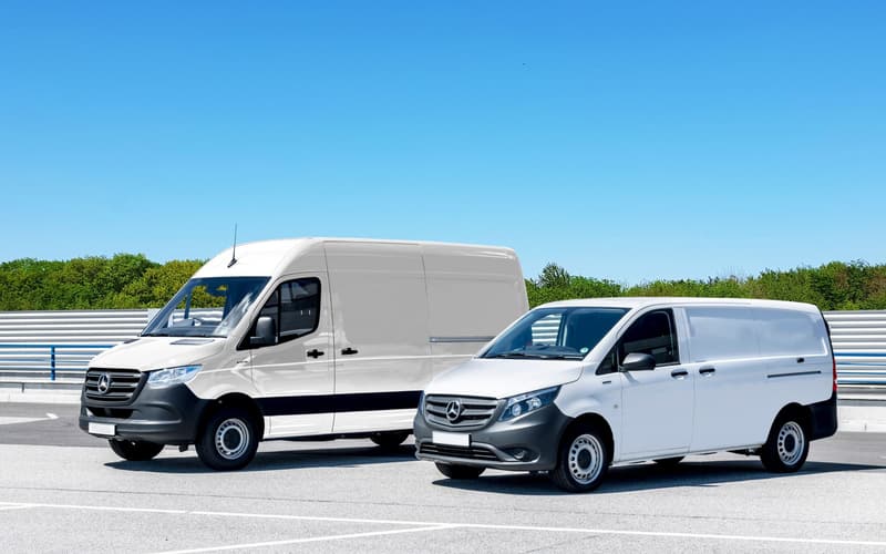 Two new white panel vans parked on a yard under a clear sky