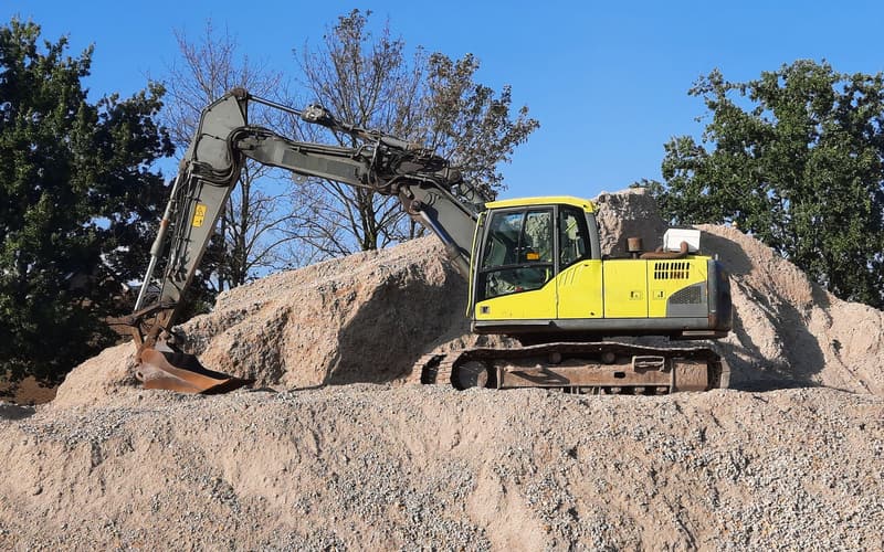 A tracked excavator standing on a mound of aggregate against blue sky
